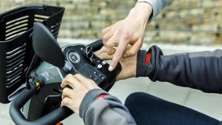 Twee handen op een scootmobiel van een medewerker in de ouderenzorg en een oudere.