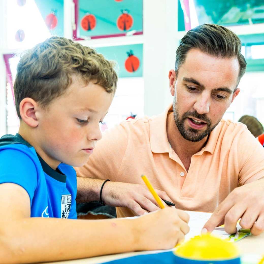 Omscholer van de pabo legt in de klas iets uit aan een leerling.