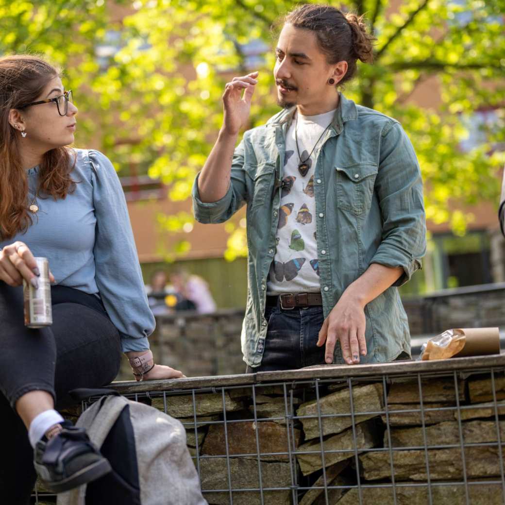 Twee studenten, jongen en meisje, zitten buiten bij K33 en kletsen met elkaar. 