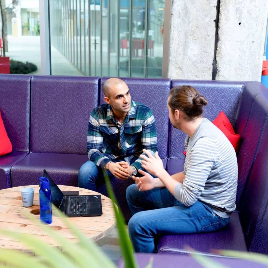 Twee post-hbo cursisten met elkaar in gesprek op een paarse bank op de HAN-campus in Arnhem.