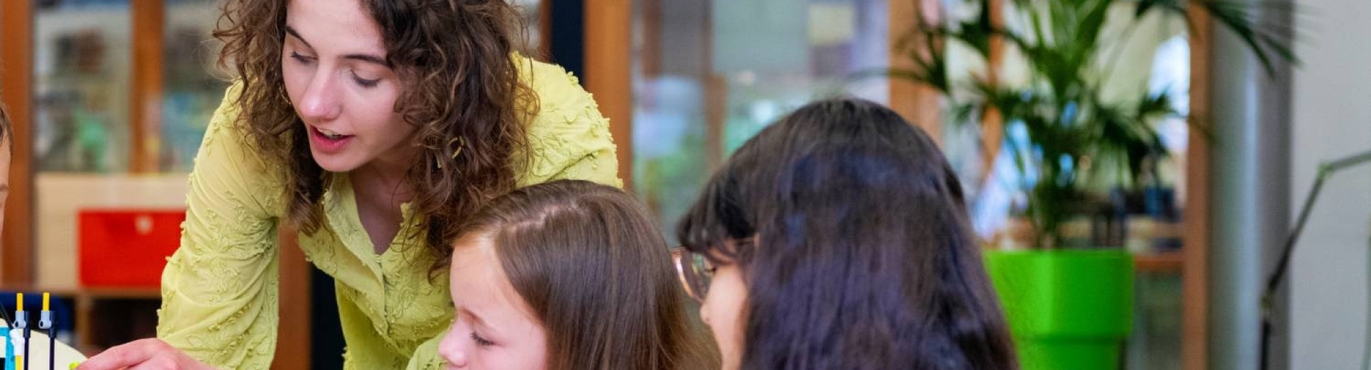Een student heeft speelgoed vast, terwijl de kinderen toekijken.