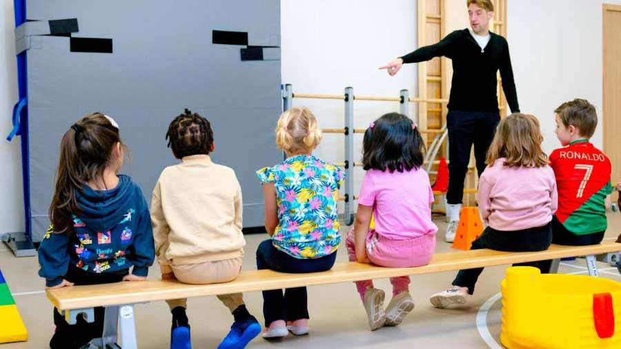 De kleuters op de school De Ommelander. De leraar wijst de kleuters iets aan in de gymzaal. 
