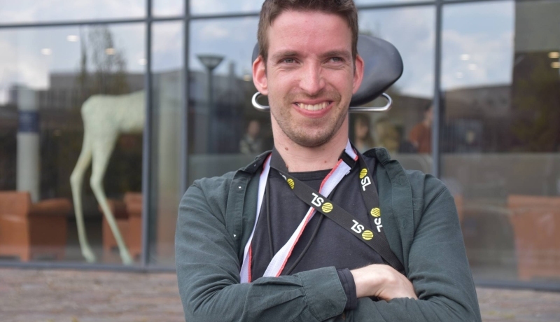 Foto van Rob Jacobs in zijn rolstoel met een donkere hoodie. Hij lacht en heeft zijn armen over elkaar