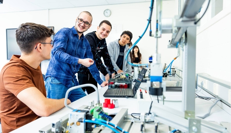 Docent en studenten elektrotechniek aan een Programmable Logic Controller (PLC).