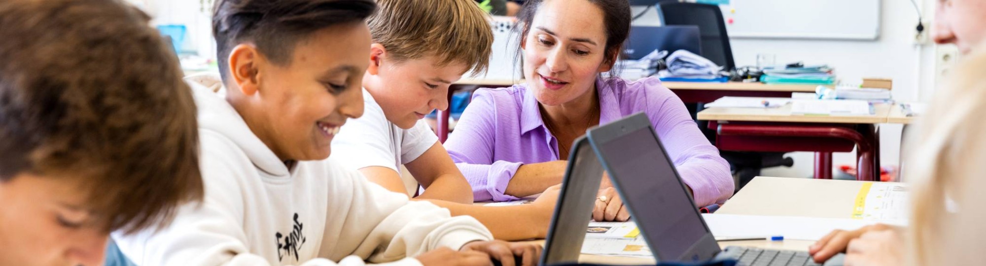 De lerares van de opleiding leraar basisonderwijs legt iets persoonlijk uit aan een leerling aan zijn tafel.