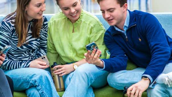 Een groep studenten zit op een groene bank samen te lachen.