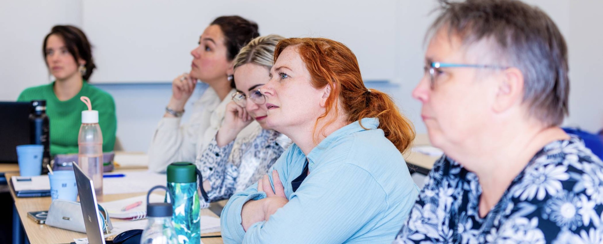 Vijf vrouwen in klaslokaal luisteren naar uitleg docent bij de opleiding technische thuiszorgverpleegkundige.