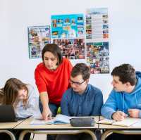 Een docente en drie studenten kijken in een boek.