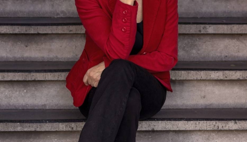 Campustheater. Debby Petters zit op een trap. Ze heeft een rood jasje aan.