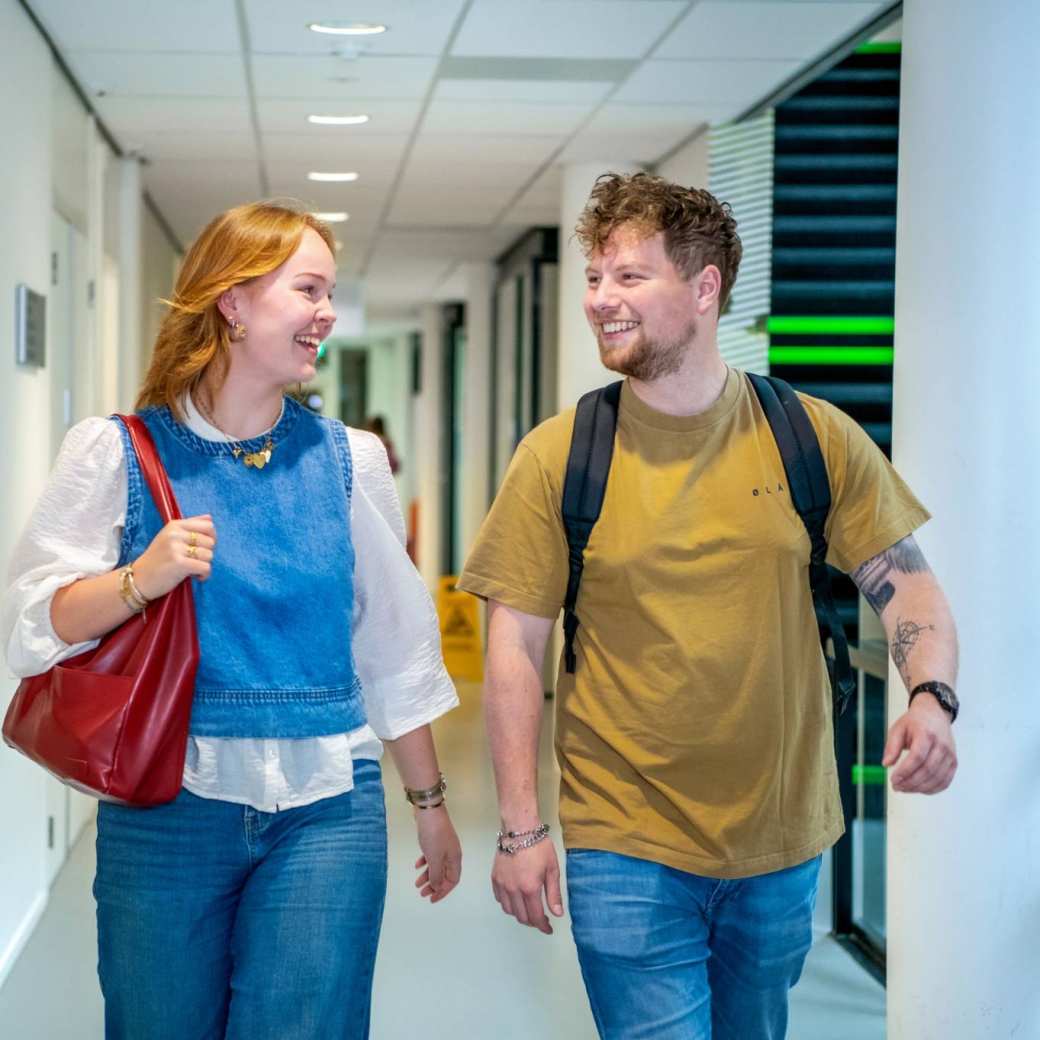 Jongen en meisje lopen in de gang op de HAN campus in Nijmegen en kijken lachend naar elkaar.