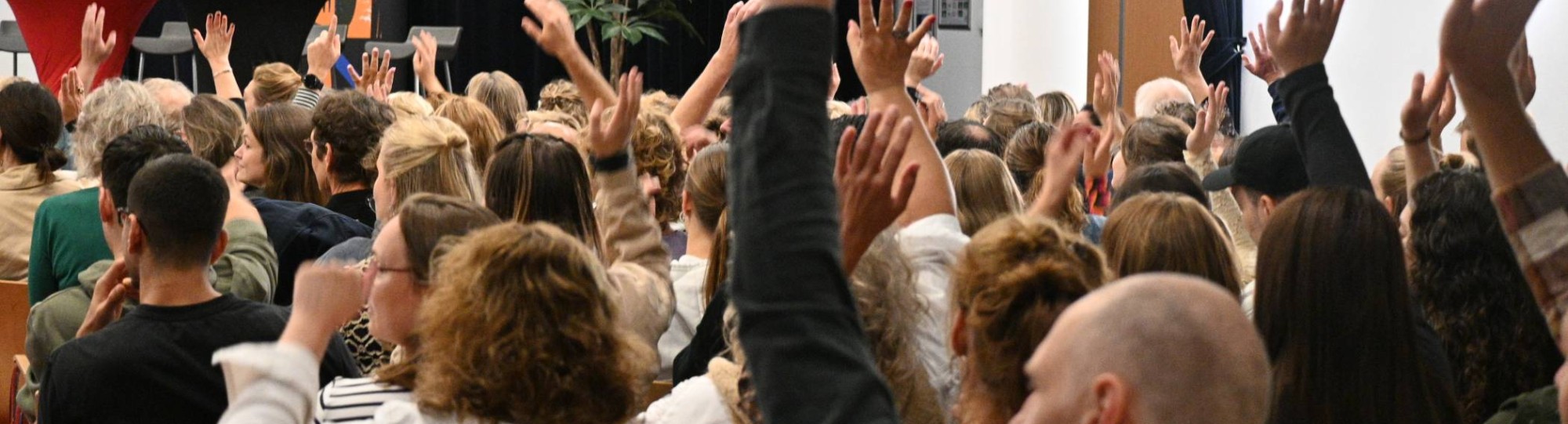 publiek met handen omhoog tijdens symposium beyond borders week tegen armoede