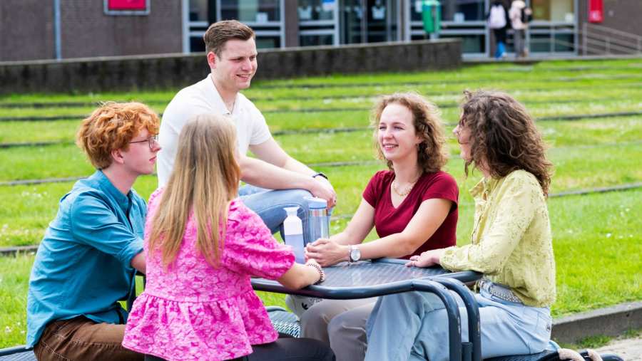 Vijf studenten zitten samen aan een tafel buiten.
