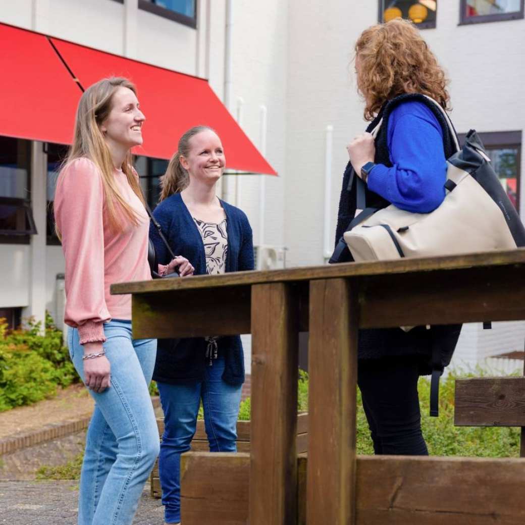 Drie vrouwen staan buiten samen te praten bij een houten railing