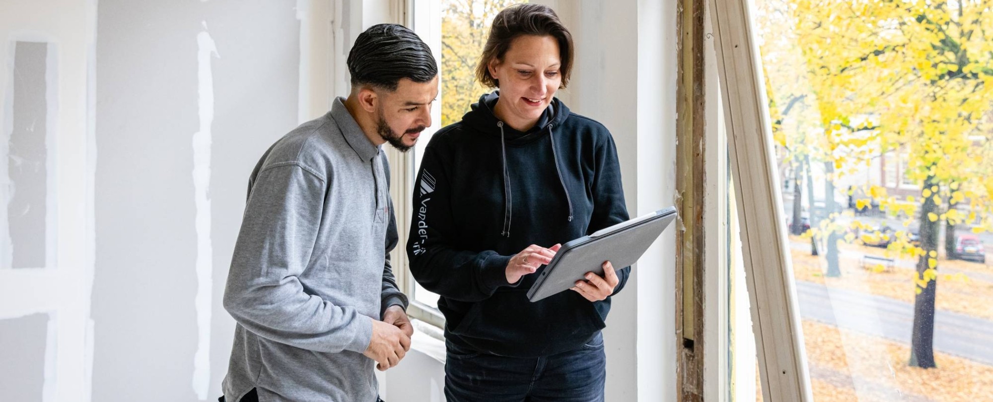 man en vrouw met bouwtekeningen in haar hand overleggen in een lege kamer die in aanbouw is.
