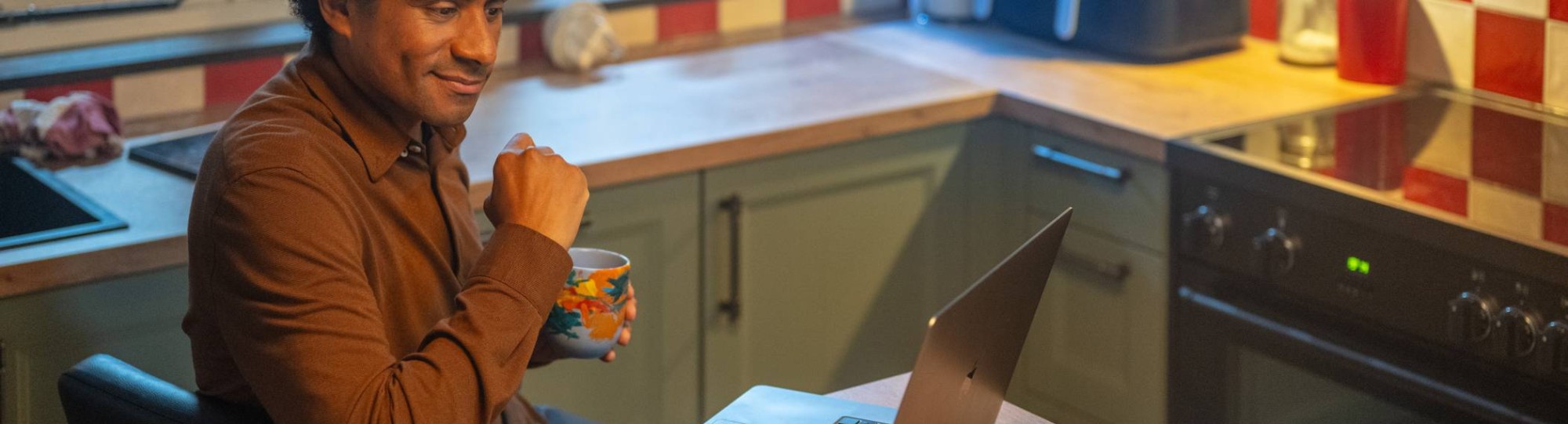 Man aan keukentafel met laptop en mok in hand