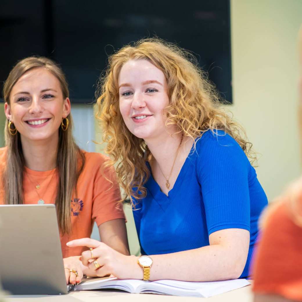 Twee studenten in gesprek met medestudenten tijdens theorieles Verpleegkunde