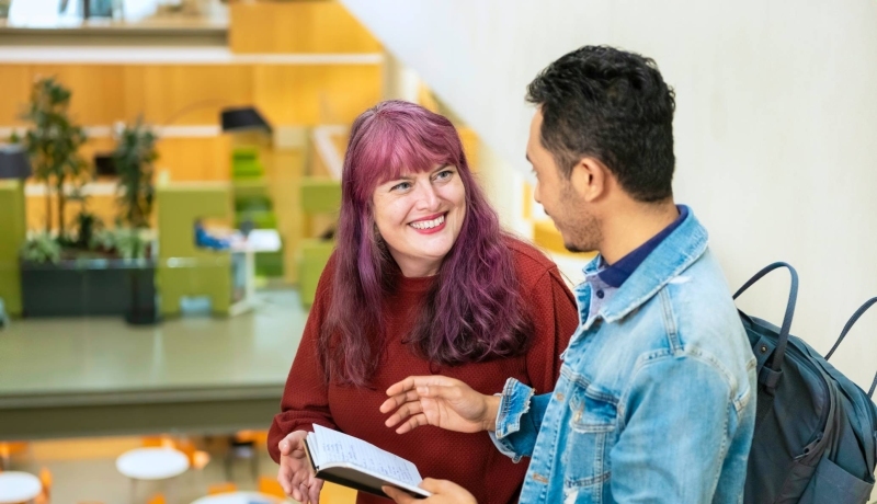 Twee studenten vertellen met elkaar terwijl de een een kladje in de hand heeft met geschreven tekst.