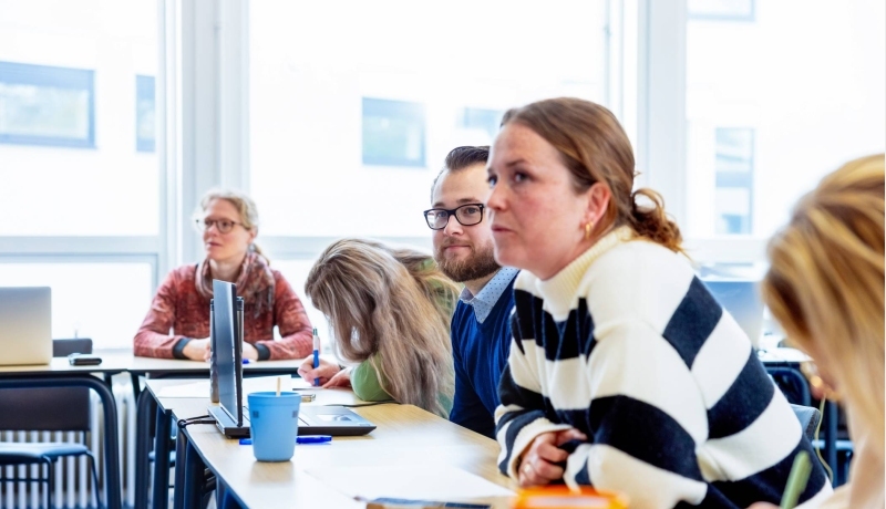 Drie mensen met elkaar pratend aan een tafel. De vrouw in de gele trui lacht tijdens het gesprek
