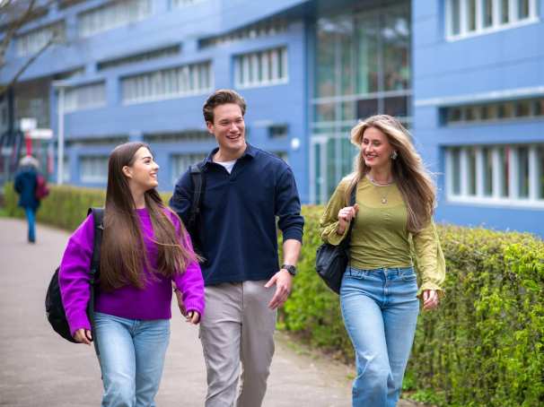 Drie studenten van Learning and Development in Organisations voltijd lopen lachend voor het HAN gebouw in Nijmegen.