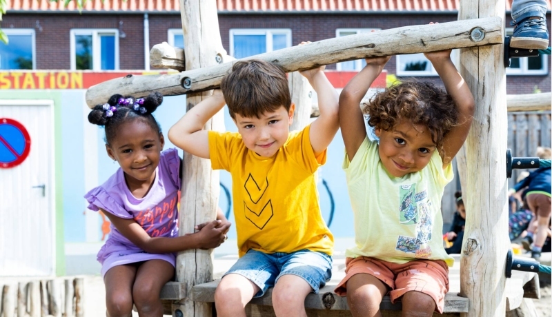 Drie kinderen spelen buiten en hangen aan het klimrek