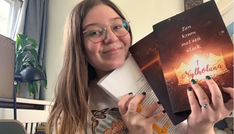 CMD-student Jade Vermeulen heeft haar eigen geschreven boeken in haar handen en glimlacht