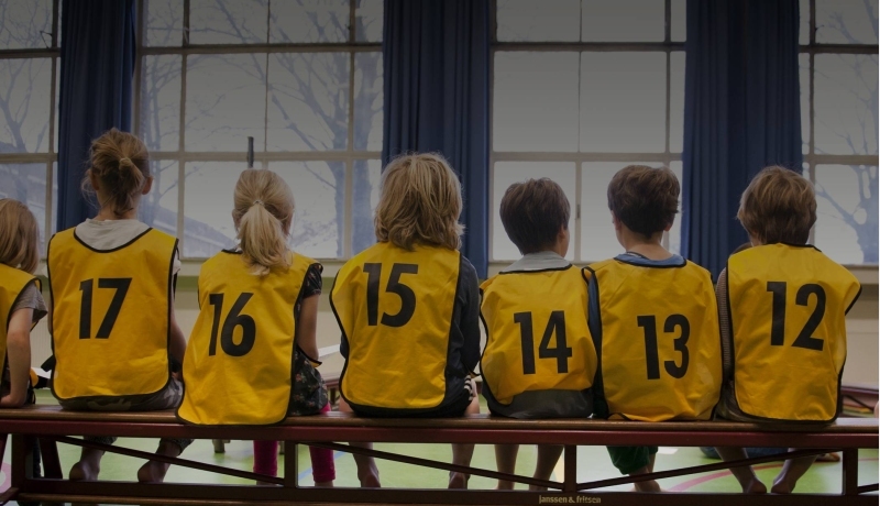 Kinderen in een gymzaal met hesjes aan op de rug gefotografeerd