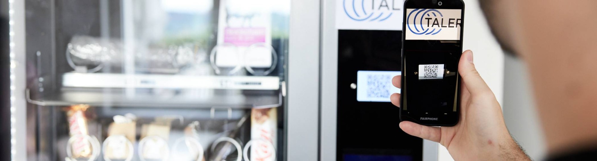 Man betaalt bij de snackautomaat met de GNU-taler app op zijn telefoon