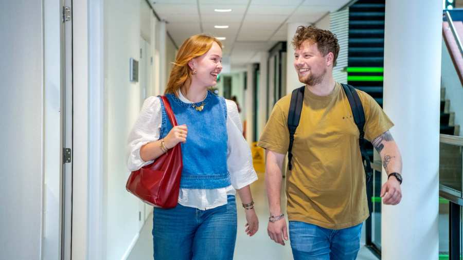 Studenten lopen op de gang op de HAN campus in Nijmegen en kijken lachend naar elkaar.