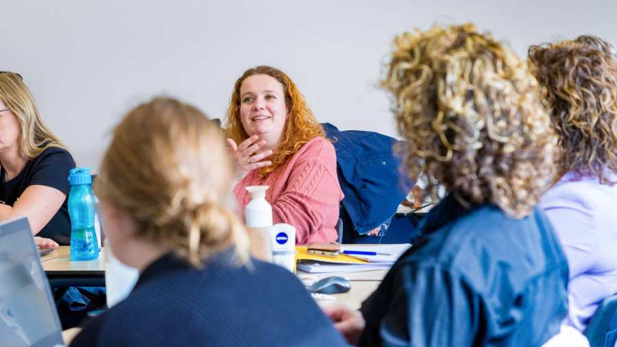 Vrouw in roze trui is in gesprek met docent tijdens de cursus acute pijn service.
