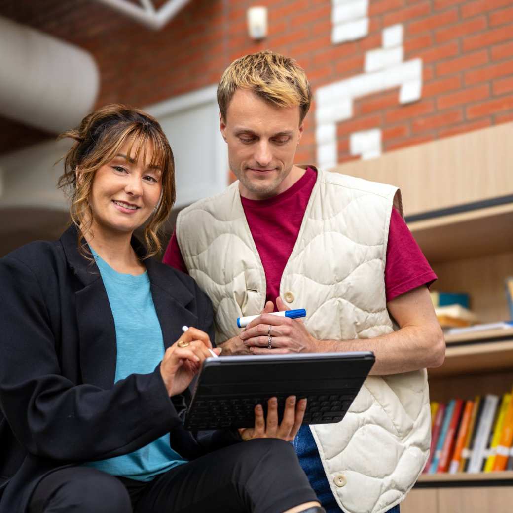Twee sudenten kijken in overleg met tablet op locatie