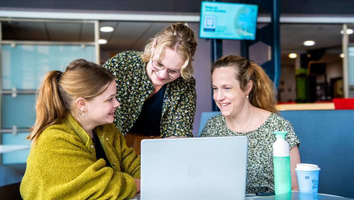 3 studenten zijn aan het overleggen met elkaar achter de laptop