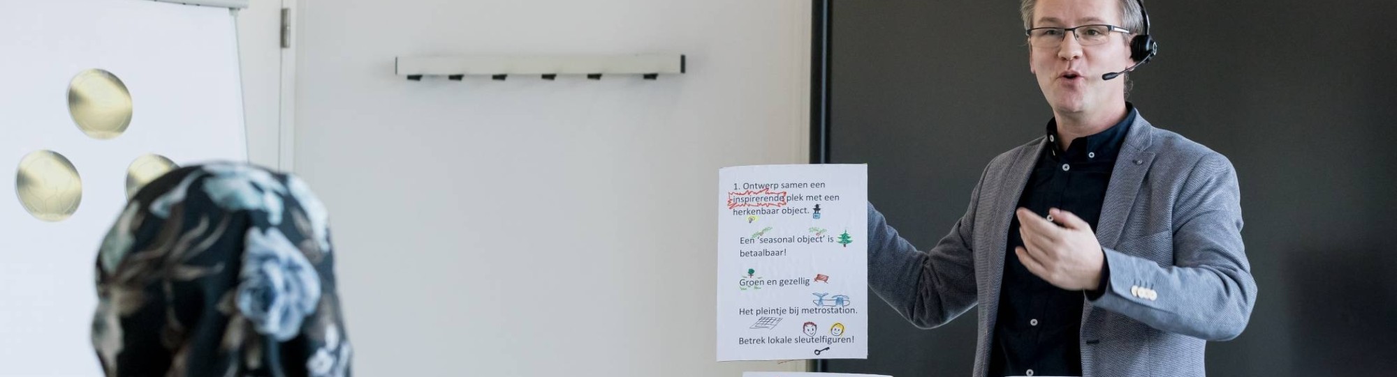 Man houdt presentatie en houdt hierbij ideeën op papier in de lucht voor de klas