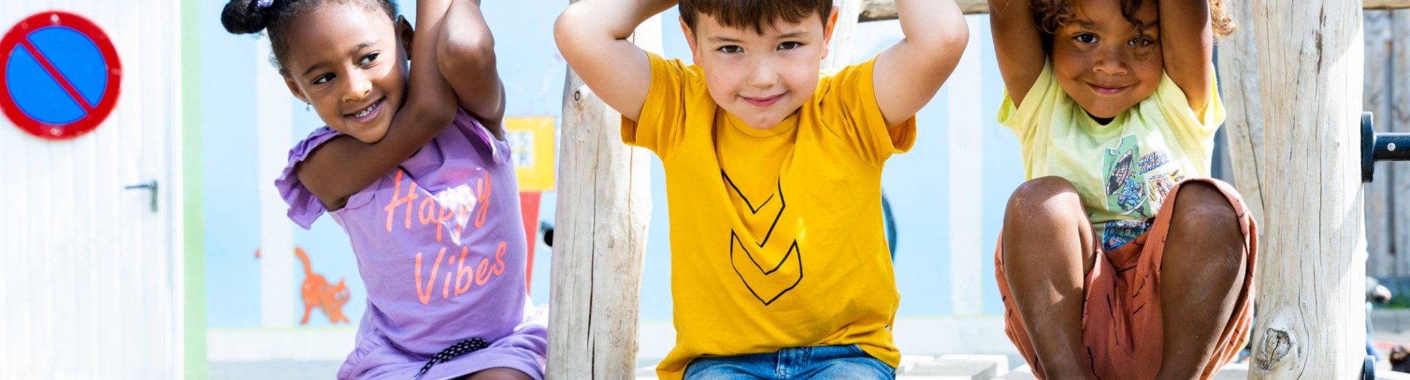 Drie kinderen spelen buiten en hangen aan het speelrek