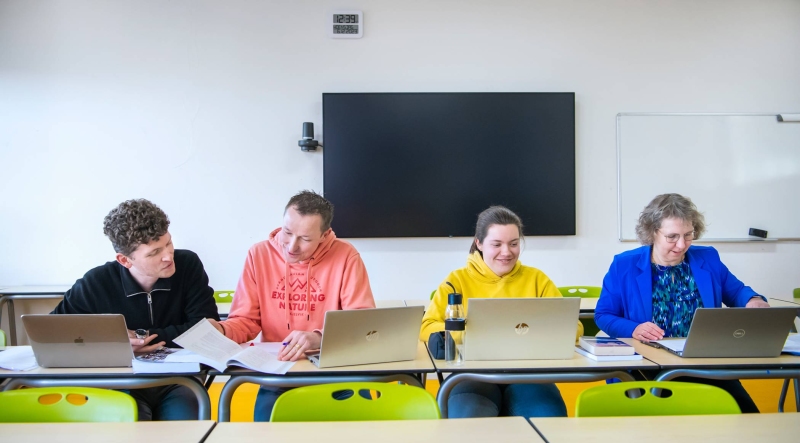 Foto Master Academie Educatie. 4 masterstudenten zitten geconcentreerd op een rij achter hun laptops aan een tafel. 