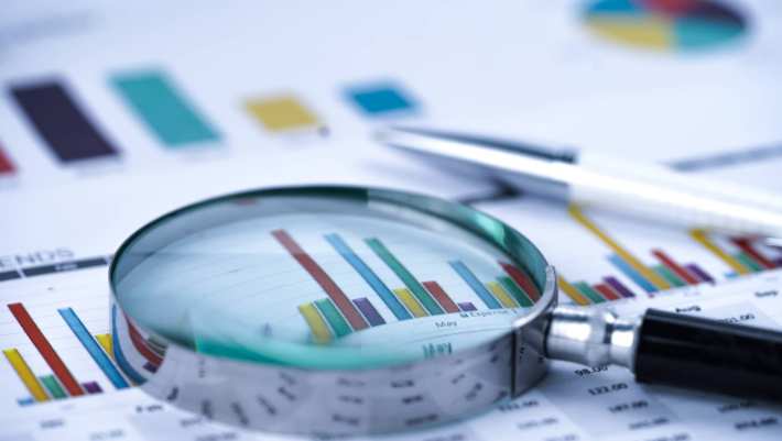 Close-up van een vergrootglas boven grafieken. Vaag een pen.