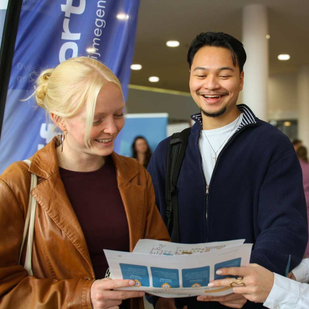 Drei studenten van de opleiding Toegepaste Psychologie in gesprek op de Netwerkmarkt van de academie Organisatie en ontwikkeling. Ze zijn lachend in gesprek en kijken naar de plattegrond van de markt.