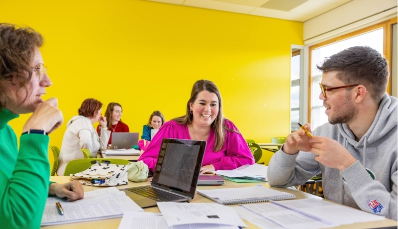 Twee studenten hbo Nederlands bladeren door een boek in de mediatheek.