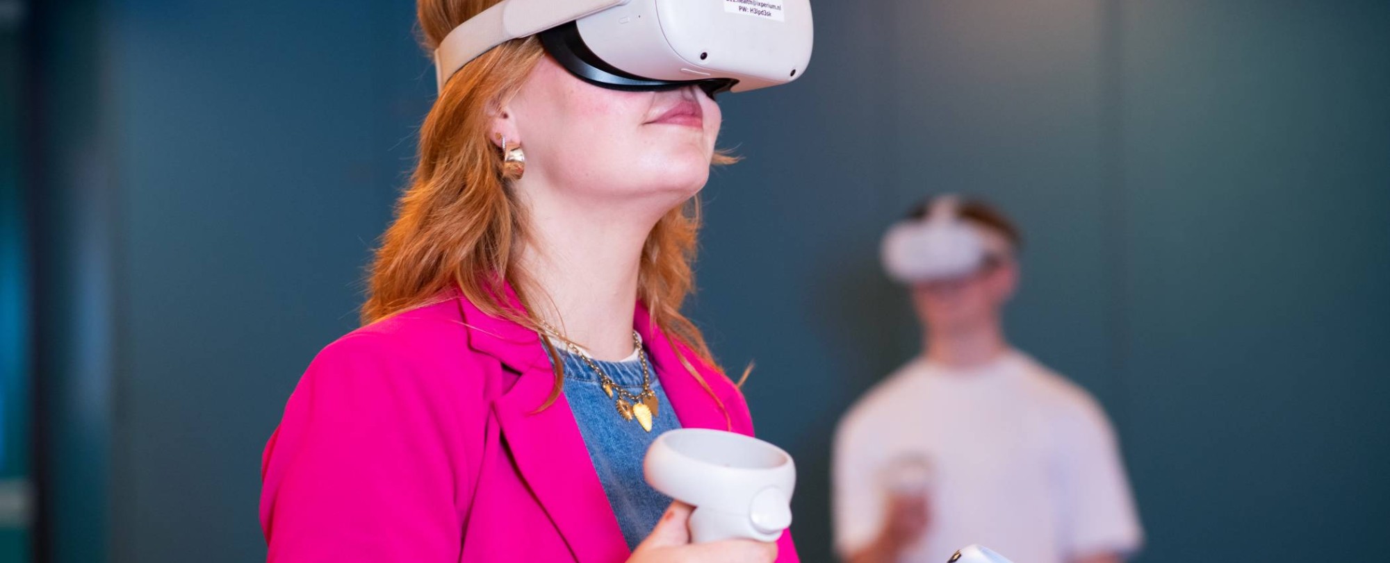 Studente oefent met VR bril, jongen wacht op de achtergrond