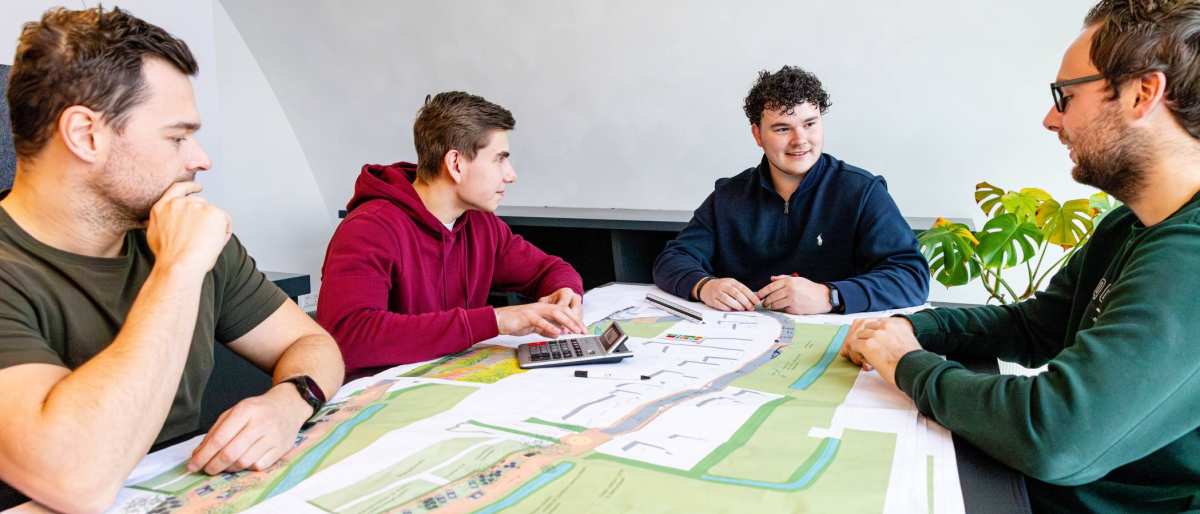 Vier mannen tijdens een bouwoverleg aan een bureau met daarop een omgevingskaart.
