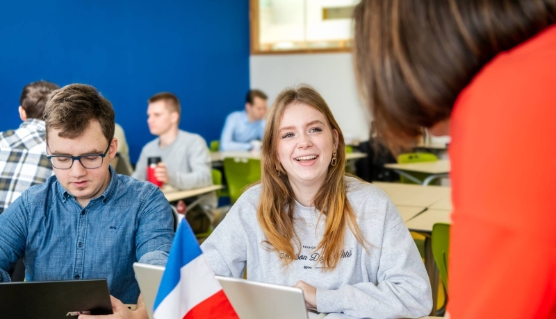 Twee studenten zitten in de mediatheek en kijken lachend naar de laptop die voor hun staat.