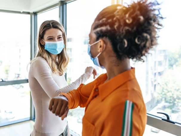 Studenten begroeten elkaar met elleboog. Mondkapjes op. Covid19. Corona