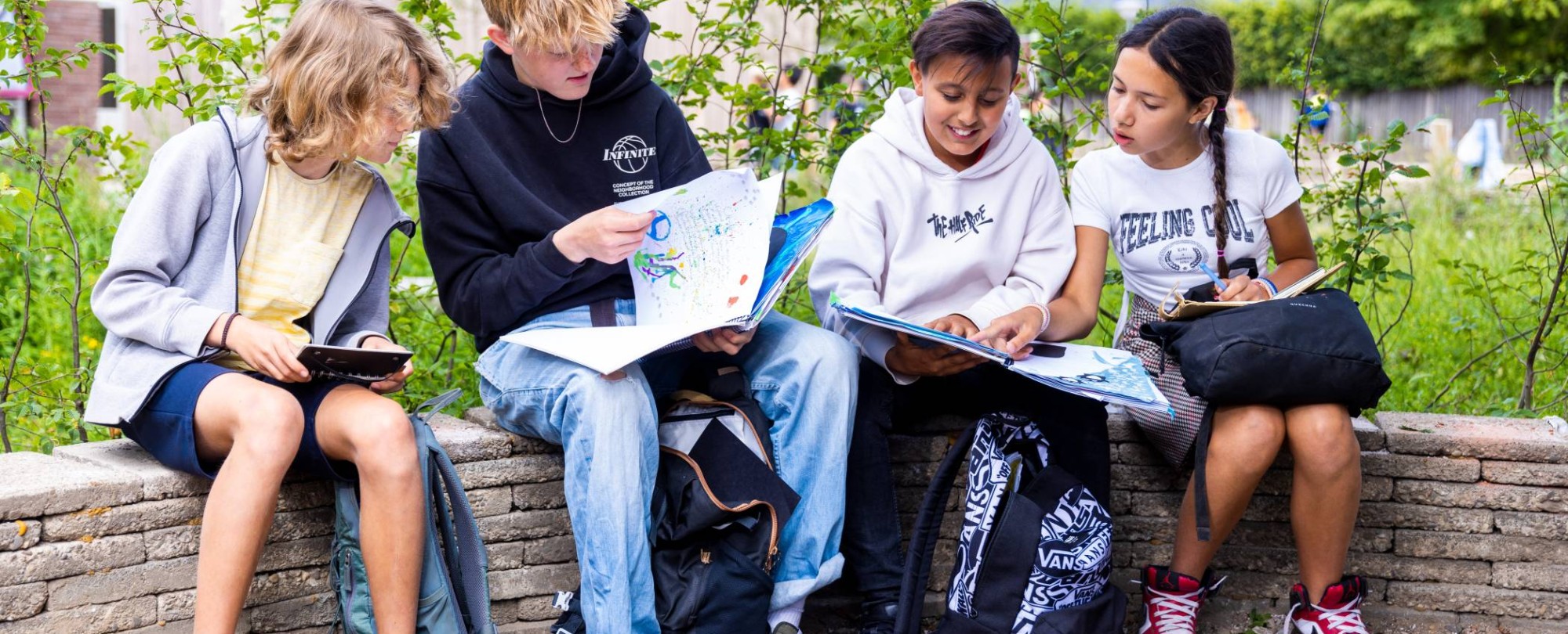 Vier leerlingen lezen buiten op een bankje. Foto van de opleiding leraar basisonderwijs