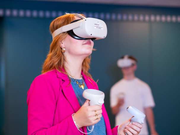 Studente oefent met VR bril, jongen wacht op de achtergrond