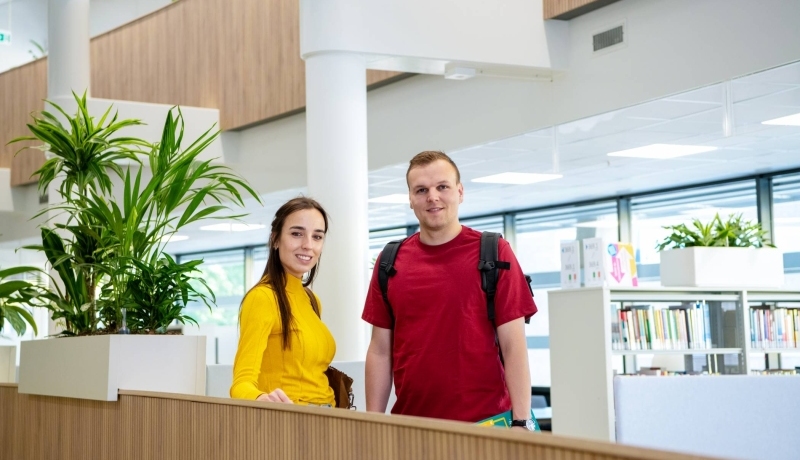 Twee studenten van de opleiding Bedrijfskunde deeltijd in gesprek in de bibliotheek in Arnhem, Ruitenberglaan 31. Ze lachen. 
