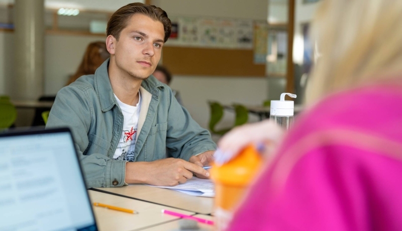 Mannelijke student in de klas luistert naar andere student. 