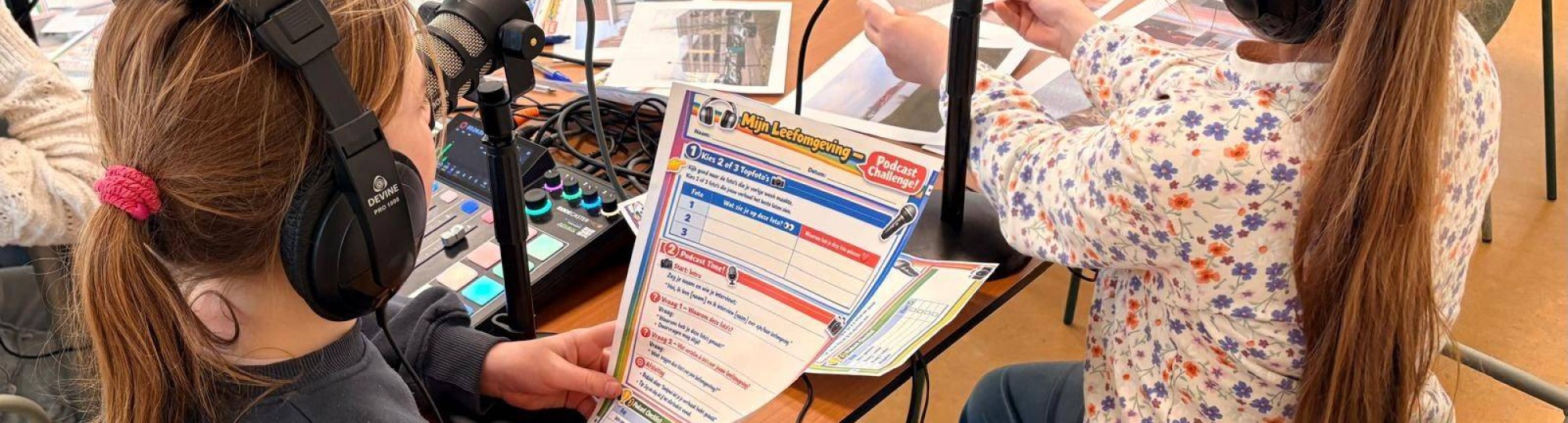 Foto van twee meisjes (met koptelefoons en foto's uit hun buurt) in gesprek met professionals over hun leefomgeving