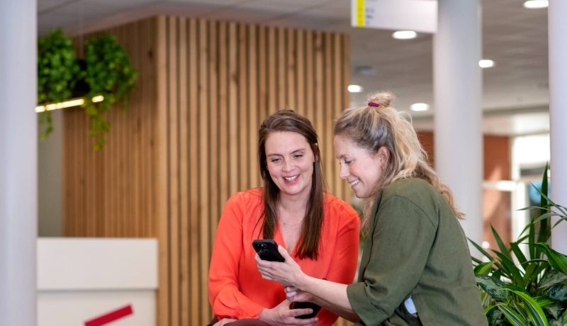 Twee deeltijdstudenten Bedrijfskunde in gesprek tijdens de pauze met een telefoon in de centrale hal van Ruitenberglaan 31.