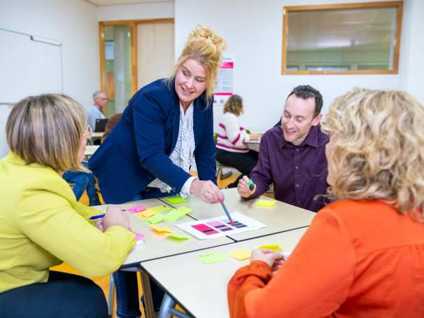 Een groepje van vier mensen in gesprek met post-its op tafel in een lokaal met anderen