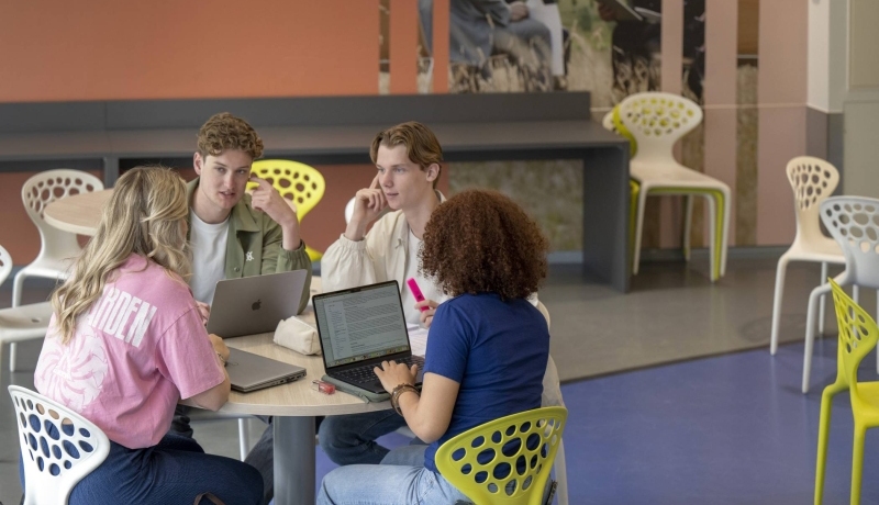 Vier studenten werken samen aan een ronde tafel in de gang in LvS10, chille werkplek.