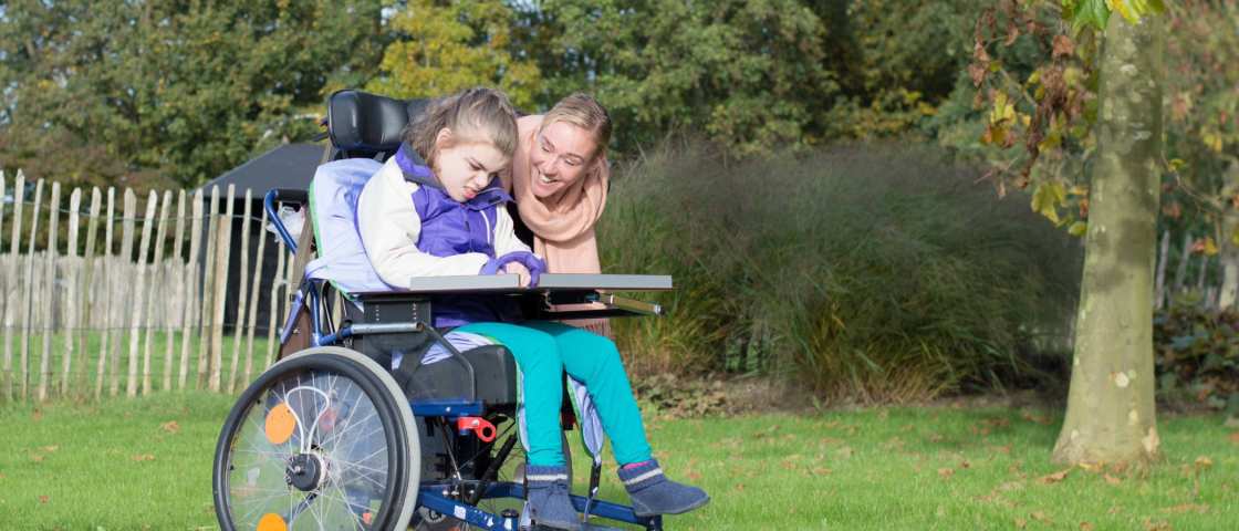 gehandicapt kind in een rolstoel buiten ontspannen samen met een verzorger